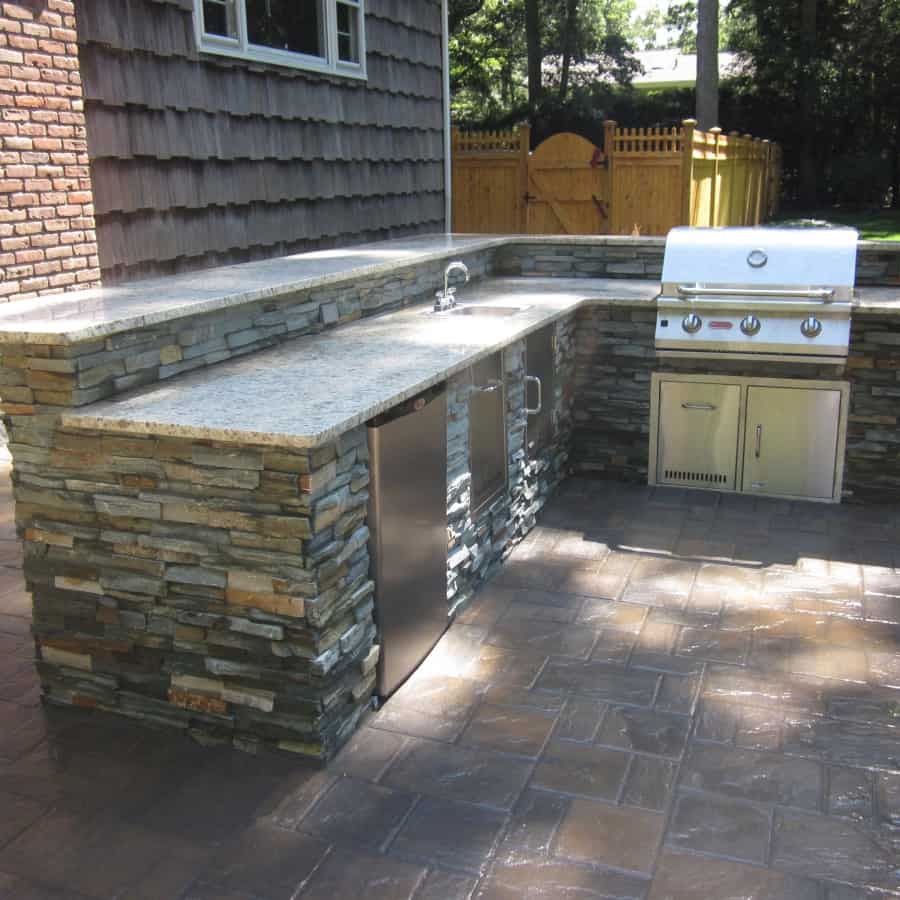 Outdoor Kitchen with Raised Bar veneered with East West Stone - Bayside Waters - Equipped with Brahma Grill, Access Doors, Sink w/ Access Door, Trash Drawer, and Refrigerator-Electrical outlets in backsplash - Dix Hills, Long Island NY